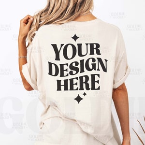 以下が含まれることがあります： 黒い文字で「YOUR DESIGN HERE」と書かれた白いオーバーサイズのTシャツ。ゆったりとしたフィット感で、あなた自身のデザインでカスタマイズするのに最適です。