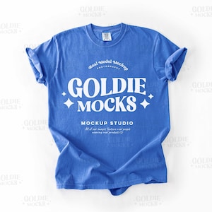 May include: A flat lay of a blue t-shirt with the text "GOLDIE MOCKS" in white. The shirt is on a white background. The text "Real Model Mockup" is also visible on the shirt.