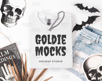May include: A white crew neck sweatshirt with the text "GOLDIE MOCKS" in black, a silver chain necklace, and a pair of distressed denim shorts. Decorative skulls and bats are arranged around the sweatshirt.
