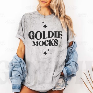 May include: A gray t-shirt with a distressed look featuring the text "Goldie Mocks" in black lettering with small black stars on either side of the text.