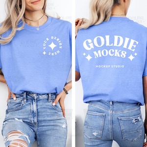 May include: A light blue t-shirt with the text "YOUR DESIGN HERE" in a white circle on the front. The back of the shirt has the text "GOLDIE MOCKS" and "MOCKUP STUDIO" in white. The model is wearing blue jeans.