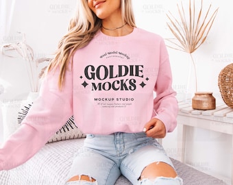 Könnte beinhalten: Ein rosafarbenes Sweatshirt mit Rundhalsausschnitt und dem Schriftzug "Goldie Mocks" in schwarzer Schrift. Das Sweatshirt hat eine lockere Passform und wird von einem Model mit langen blonden Haaren getragen.