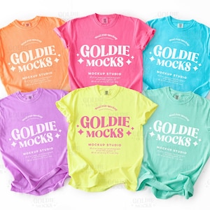 Puede incluir: Una colección de seis camisetas coloridas en tonos naranja, rosa, azul, morado, amarillo y verde menta. Cada camiseta presenta el texto "GOLDIE MOCKS MOCKUP STUDIO" en blanco y negrita.