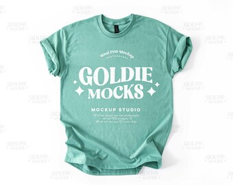 Könnte beinhalten: Ein Mockup eines tealgrünen T-Shirts mit dem Text "Goldie Mocks" und "Mockup Studio" in Weiß. Der Text ist in einem Retro-Schriftart-Stil.