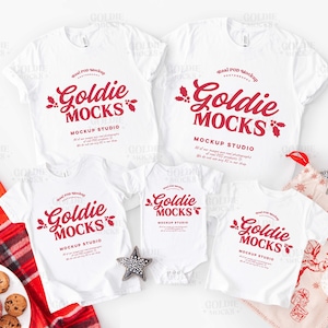 May include: A collection of white t-shirts and a babygrow, each featuring the red text "Goldie Mocks" with holly. The mockup includes a star decoration and a Christmas stocking, suggesting a festive theme.