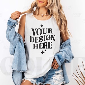 May include: A white tank top with the text "YOUR DESIGN HERE" in black lettering. The tank top is being worn by a person with long blonde hair and a denim jacket.
