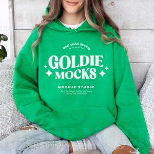 May include: A bright green hoodie with a white graphic that reads "GOLDIE MOCKS" and "MOCKUP STUDIO". The hoodie has a front pocket and a drawstring hood. The text "Real Model Mockup" is above the main text.