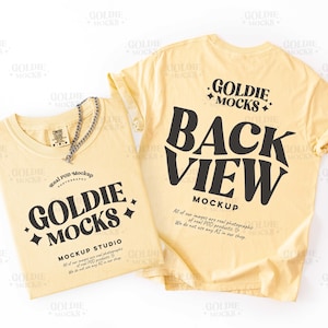 May include: Two light yellow t-shirts, one folded and one unfolded, with black text that reads "GOLDIE MOCKS" and "BACK VIEW MOCKUP". A silver chain necklace rests on the folded shirt. The shirts are on a white background.