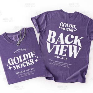 May include: Two purple t-shirts with white text and a silver chain necklace. One shirt displays "GOLDIE MOCKS" and "MOCKUP STUDIO". The other shirt reads "BACK VIEW MOCKUP". The shirts are on a white background.
