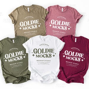 May include: Four t-shirts in different colors, olive green, white, maroon, and heather gray, with the text "Goldie Mocks Mockup Studio" printed on the front.