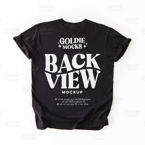 Op de afbeelding: Zwarte t-shirt mockup met de tekst "GOLDIE MOCKS" en "BACK VIEW" in wit. De tekst "MOCKUP" staat ook in wit onder de hoofdtekst.