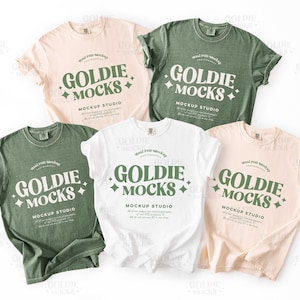 Può includere: Cinque magliette in vari colori: rosa chiaro, verde salvia, bianco e due tonalità di verde. Ogni maglietta presenta il testo "GOLDIE MOCKS" in un font stilizzato con un design a diamante. Sono visibili anche le parole "MOCKUP STUDIO".