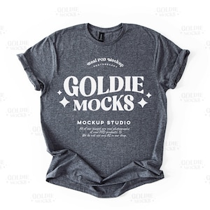 Könnte beinhalten: Ein dunkelgraues T-Shirt mit einem weißen Grafikdesign, auf dem "Real POD Mockup Photography Goldie Mocks + Mockup Studio" steht. Der Text ist in einem Retro-Schriftart-Stil.