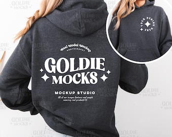 May include: A dark gray hooded sweatshirt with a white logo that says "Goldie Mocks" and "Mockup Studio". The logo is in a retro font style. The sweatshirt is being worn by a person with long brown hair.