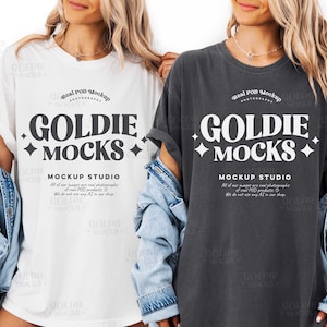 May include: Two t-shirts, one white and one charcoal grey, each featuring the text "GOLDIE MOCKS" in a bold, stylized font. The shirts are part of a mockup studio, as indicated by the text below the main text.