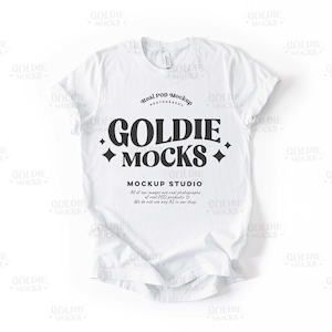 May include: White t-shirt mockup featuring the text "Goldie Mocks" in a retro font. The text is surrounded by small diamond shapes. The text "Real POD Mockup Photography" is above the main text. Below the main text is the text "Mockup Studio" and the text "All of our images are real photographs of real POD products. We do not use any AI in our shop."
