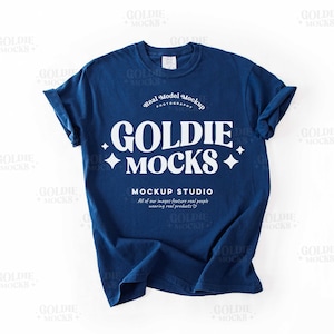 以下が含まれることがあります： 白いグラフィックで「Goldie Mocks」と「Mockup Studio」と書かれたネイビーブルーのTシャツ。テキストはレトロなフォントスタイルです。