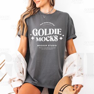Może przedstawiać: Szary t-shirt z białym nadrukiem "GOLDIE MOCKS MOCKUP STUDIO".
