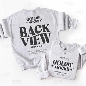 May include: Two light gray sweatshirts with white cuffs are displayed. The larger sweatshirt has the text "BACK VIEW MOCKUP" in black. The smaller sweatshirt has the text "GOLDIE MOCKS MOCKUP STUDIO" in black. The sweatshirts are on a white background.