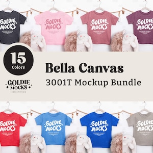 May include: A mockup bundle of Bella Canvas 3001T t-shirts in various colours, displayed on hangers. The shirts are in shades of grey, pink, red, blue, and more. The text "Goldie Mocks" is printed on each shirt. The image also includes the text "15 Colors" and "Bella Canvas 3001T Mockup Bundle."