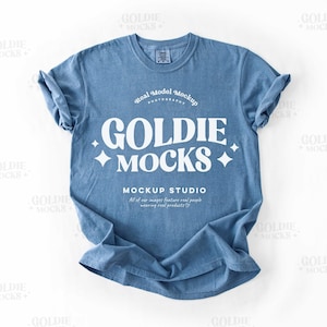 Puede incluir: Una maqueta de camiseta azul con el texto "GOLDIE MOCKS" y "MOCKUP STUDIO" impreso en la parte delantera. El texto es blanco y la camiseta está arrugada.