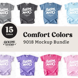 Op de afbeelding: Een mockup-bundel van Comfort Colors t-shirts in verschillende kleuren, waaronder grijs, zwart, blauw en roze. Elk shirt toont het witte "Goldie Mocks" logo. De afbeelding bevat ook tekst met 15 kleuren en de "9018 Mockup Bundle."