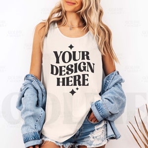 May include: A white tank top with the text "YOUR DESIGN HERE" in black. The tank top is being worn by a person with long blonde hair and a denim jacket.