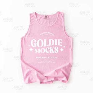 May include: A light pink tank top with the text "GOLDIE MOCKS" in white, along with the words "MOCKUP STUDIO". The tank top is a solid color and has a simple, classic design.