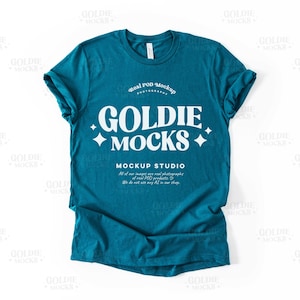 Pode incluir: Uma camiseta azul turquesa com um gráfico branco que diz "Goldie +Mocks" e "Mockup Studio". O texto está em um estilo de fonte retrô.