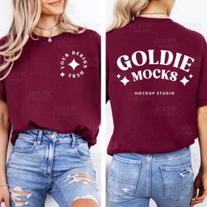 以下が含まれることがあります： 前面に「Your Design Here」と星が書かれた白いデザイン、背面に「Goldie Mocks」と星と「Mockup Studio」の文字が書かれた白いデザインが施された、マルーンのTシャツのモックアップです。
