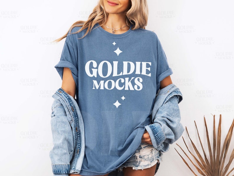 May include: A blue t-shirt with the text "Goldie Mocks" in white lettering. The shirt has a distressed look and features small white stars.