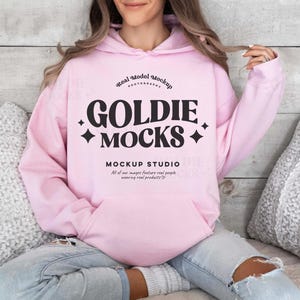 Op de afbeelding: Een roze hoodie met een zwarte afbeelding die "Real Model Mockup Photography Goldie Mocks Mockup Studio All of our images feature real people wearing real products." zegt.