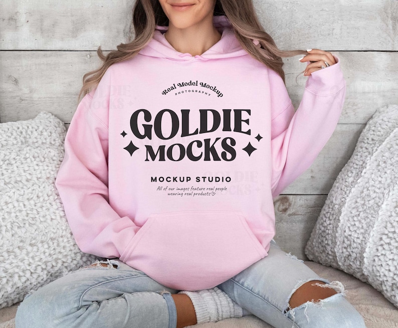 Op de afbeelding: Een roze hoodie met een zwarte afbeelding die "Real Model Mockup Photography Goldie Mocks Mockup Studio All of our images feature real people wearing real products." zegt.