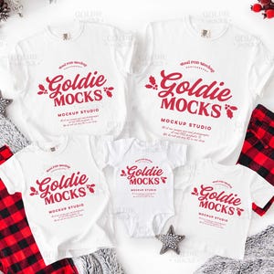 Puede incluir: Una maqueta con camisetas blancas y un body con el texto "Goldie Mocks" en rojo, junto con pantalones de pijama a cuadros rojos y negros. También hay un adorno en forma de estrella y bayas decorativas.