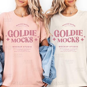 May include: Two women wearing t-shirts with the text "GOLDIE MOCKS" in pink. The shirts are different colors, one is light pink and the other is off-white. Both shirts have the text "MOCKUP STUDIO" below the main text.