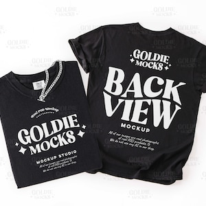May include: Two black t-shirts with white text. One shirt is folded, displaying "GOLDIE MOCKS" and "MOCKUP STUDIO." The other shirt shows "BACK VIEW MOCKUP." A silver chain necklace rests on the folded shirt. The shirts are on a white background.
