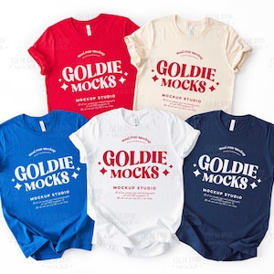 以下が含まれることがあります： 赤、ベージュ、青、白、紺色の5種類のTシャツ。それぞれに「Goldie Mocks」と「Mockup Studio」の文字がプリントされています。