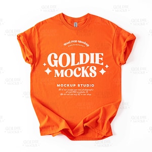 May include: Orange t-shirt mockup with the text "Goldie Mocks" and "Mockup Studio" in white. The text is in a retro font style.
