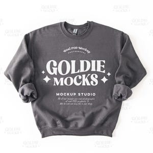 May include: A gray sweatshirt with the text "Goldie Mocks" and "Real POD Mockup" printed on the front. The text is in a white, bold font.