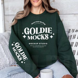 May include: A dark green sweatshirt with white text that reads "Real POD Mockup Goldie Mocks Mockup Studio All of our images feature real people wearing real products Goldie Mocks".