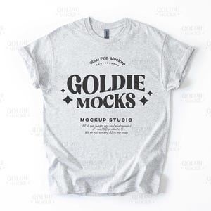 May include: A gray t-shirt mockup with the text "Goldie Mocks" in a black retro font. The text is surrounded by small diamond shapes. The text "Real Pod Mockup Photography" is above the main text and the text "Mockup Studio" is below the main text. The text below the main text reads "All of our images are real photographs of real POD products. We do not use any AI in our shop."