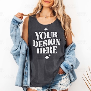 Puede incluir: Un tanque sin mangas de color gris oscuro con el texto "YOUR DESIGN HERE" en blanco. El tanque está siendo usado por una persona con cabello largo rubio y una chaqueta de mezclilla.