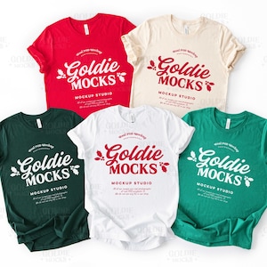May include: A mockup of five t-shirts in red, cream, white, green, and dark green. Each shirt displays the text "Goldie Mocks Mockup Studio" in a contrasting colour. The shirts are arranged on a white background.