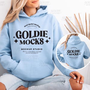Peut inclure: Un sweat à capuche bleu clair avec un logo noir qui dit "Goldie Mocks" et "Mockup Studio". Le logo est dans une police de caractères de style rétro. Le sweat à capuche est porté par une personne.