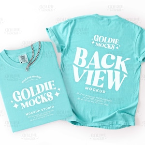 Puede incluir: Dos camisetas turquesas, una doblada y otra mostrando la vista trasera. La camiseta doblada tiene un collar de cadena plateada. Ambas camisetas muestran el texto "GOLDIE MOCKS" en blanco, con texto adicional que indica un estudio de maqueta.