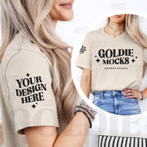 May include: Two women wearing beige t-shirts with the text "Goldie Mocks" and "Your Design Here" printed on them. The t-shirts are a mockup for a design studio.