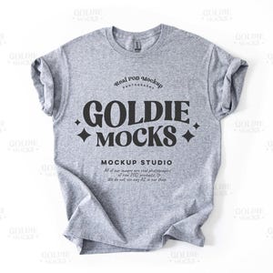 May include: A gray t-shirt mockup with the text "Goldie Mocks" in black lettering. The text "Real POD Mockup Photography" and "Mockup Studio" are also included in smaller font sizes.