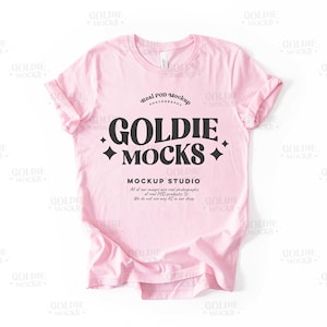 May include: A pink t-shirt mockup with the text "Goldie Mocks" and "Mockup Studio" in black. The text also includes the phrase "Real Pop Mockup Photography".