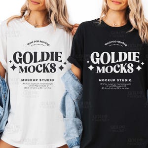 May include: Two t-shirts, one white and one black, each with the text "GOLDIE MOCKS" in a bold, stylized font. The shirts are part of a mockup studio, as indicated by the text below the main logo. Both shirts are worn with a denim jacket.