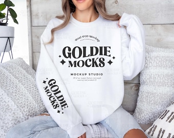 May include: White sweatshirt with long sleeves and a crew neck. The sweatshirt has black text that reads "Real POD Mockup Goldie MOCKS + Mockup Studio All of our images feature real people wearing real products."  The text "GOLDIE MOCKS +" is in a larger font size and is repeated on the sleeves.